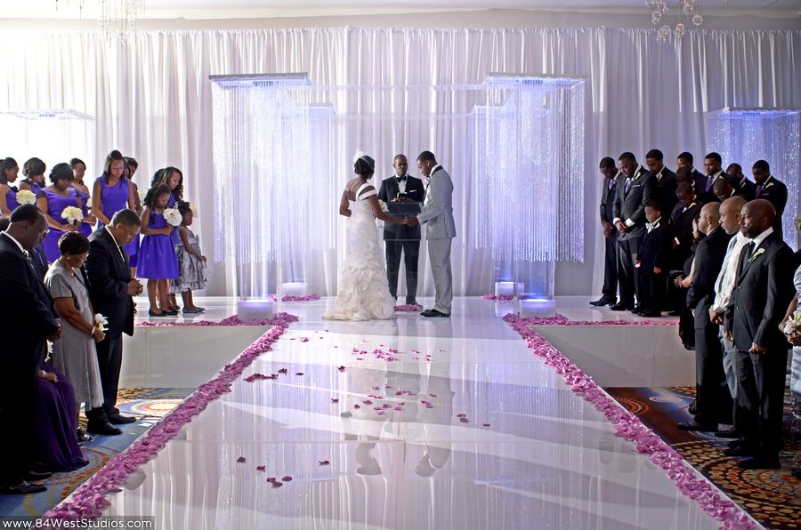 Posh wedding ceremony decor featuring crystal backdrop and wide aisle decorated with lavender purple rose petals.